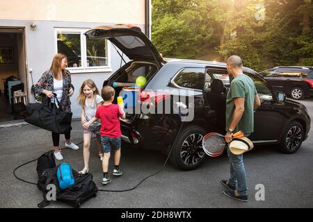 Famille avec bagages et voiture électrique noire dans la cour arrière Banque D'Images