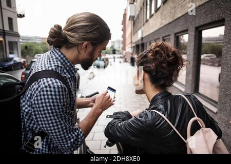 Homme montrant un smartphone à un ami sur le trottoir de la ville Banque D'Images