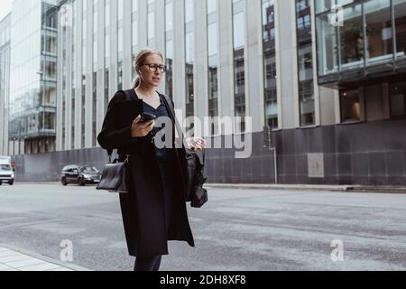 Femme d'affaires qui envisage de marcher avec un smartphone en ville Banque D'Images