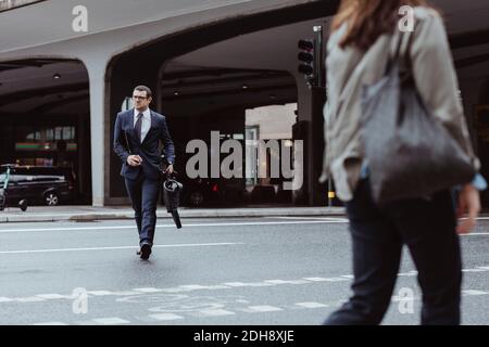 Entrepreneur avec sac et smartphone traversant la route en ville Banque D'Images