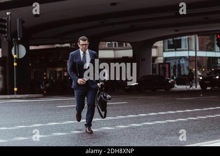 Homme d'affaires avec sac et smartphone traversant la route en ville Banque D'Images