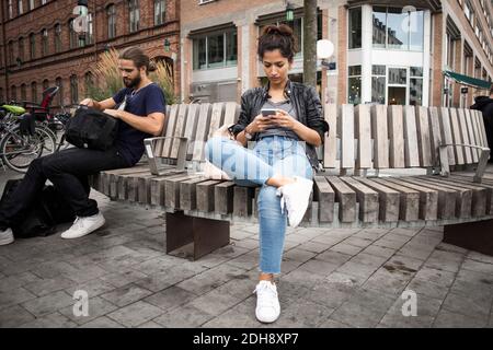 Vue à angle bas de l'homme et de la femme assis sur du bois banc contre bâtiment en ville Banque D'Images