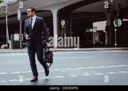 Homme d'affaires avec sac et parapluie traversant la route en ville Banque D'Images