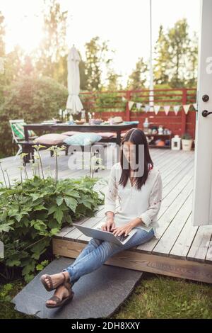 Femme utilisant un ordinateur portable tout en étant assise sur le plancher à la terrasse dans arrière-cour Banque D'Images