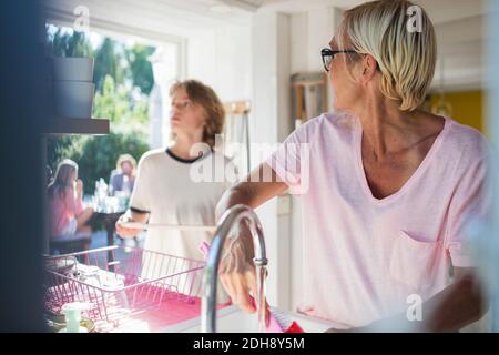 Femme regardant un fils adolescent debout tout en lavant des assiettes cuisine Banque D'Images