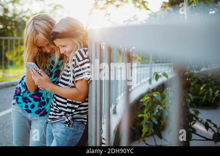 Des amis heureux en utilisant un téléphone portable tout en se penchant sur la main courante Banque D'Images