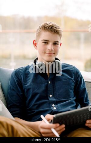 Portrait d'un adolescent souriant avec tablette numérique sur le canapé à la maison Banque D'Images