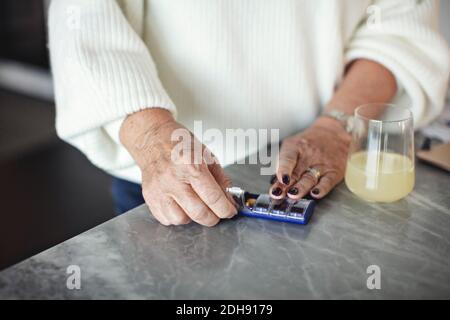 Section médiane de la femme âgée prenant des pilules à la maison Banque D'Images