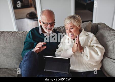 Couple senior souriant utilisant une tablette numérique tout en étant assis sur un canapé dans la salle de séjour Banque D'Images