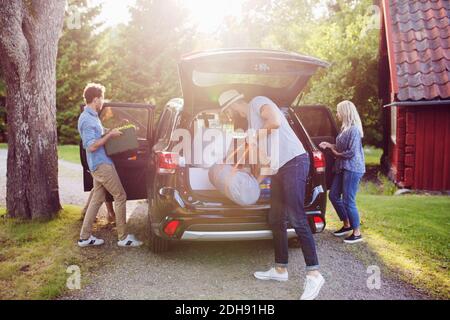 Des amis qui chargent leurs bagages en voiture sur la route par beau temps Banque D'Images