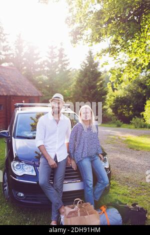 Portrait de l'homme et de la femme avec les bagages inclinant sur la voiture contre les arbres Banque D'Images