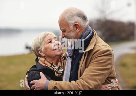 Couple senior souriant s'embrassant les uns les autres au bord du lac Banque D'Images