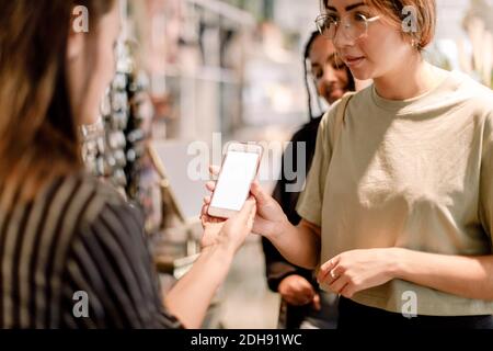 Femme montrant le téléphone à la vendeuse dans un magasin de mode Banque D'Images