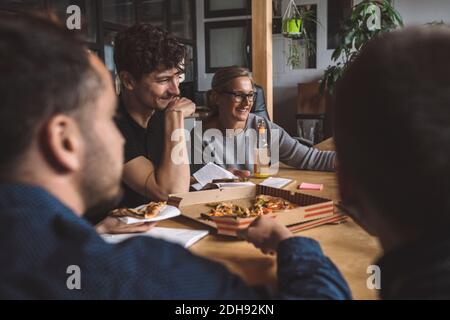 Collègues souriants qui mangent de la pizza sur le lieu de travail Banque D'Images