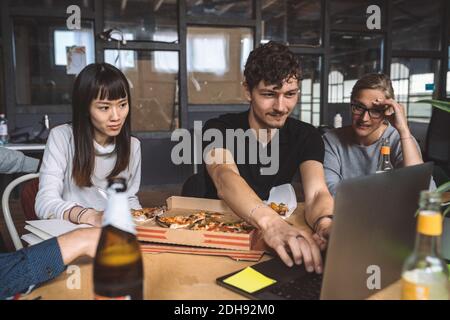 Des collègues souriants qui travaillent avec des pizzas sur leur lieu de travail Banque D'Images