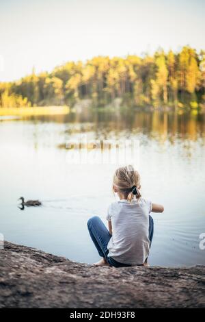 Vue arrière d'une fille assise sur un rocher au lac Banque D'Images