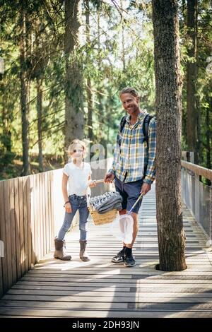 Portrait du père et de la fille avec panier de pique-nique debout passerelle en forêt Banque D'Images