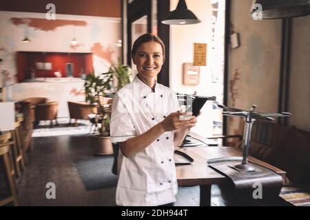 Portrait d'un chef souriant avec un smartphone dans le restaurant Banque D'Images