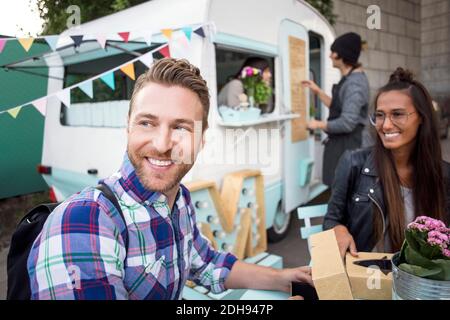 Clients heureux assis à la table pendant que les propriétaires de camions alimentaires travaillent en arrière-plan Banque D'Images