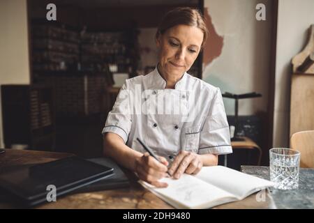 Chef cuisinier mature écrivant dans le livre au restaurant Banque D'Images