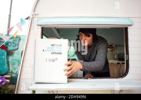 Le propriétaire qui regarde loin en plaçant l'affiche à la fenêtre camion alimentaire Banque D'Images