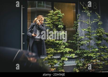 Femme d'affaires de taille moyenne utilisant un appareil mains libres en traversant la rue Banque D'Images