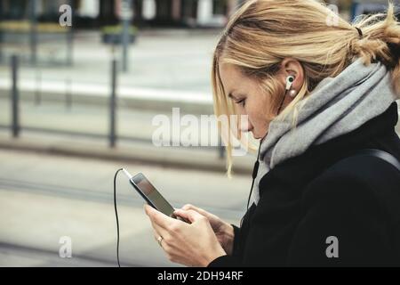 Vue latérale d'une femme d'affaires utilisant un smartphone à la station de tramway Banque D'Images