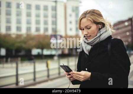 Femme d'affaires de taille moyenne qui écoute de la musique par téléphone intelligent en tram station Banque D'Images