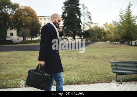 Vue latérale d'un homme d'affaires de taille moyenne qui parle sur un téléphone portable en marchant sur le trottoir Banque D'Images