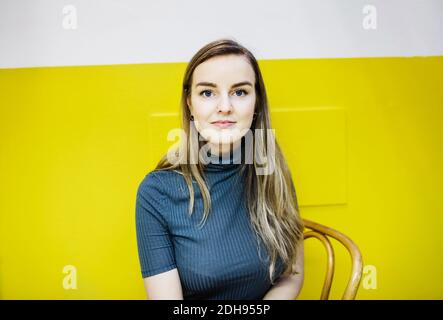 Portrait d'une jeune femme confiante assise contre un mur jaune bureau Banque D'Images