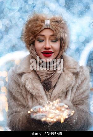 Femme en vêtements d'hiver tenant la lumière de Noël par temps froid Banque D'Images