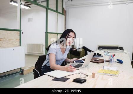 Jeune femme écrivant tout en travaillant à un bureau dans le bureau Banque D'Images