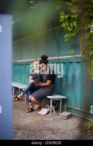 Pleine longueur de jardiniers avec tablette numérique assis sur le banc dans la cour Banque D'Images