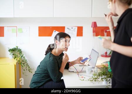 Femme d'affaires utilisant un appareil mains libres tout en regardant un collègue au bureau Banque D'Images