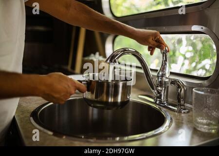 Section centrale de l'homme remplissant l'eau par le robinet de la remorque de camping Banque D'Images