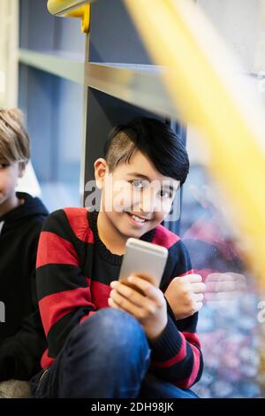 Portrait d'un garçon souriant tenant un smartphone au collège Banque D'Images