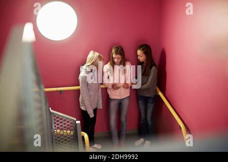 Fille utilisant un téléphone mobile avec des amis contre le mur rose dedans école secondaire Banque D'Images