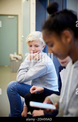 Garçon d'école moyenne ennuyé assis avec des amis dans le couloir Banque D'Images