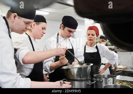 Enseignant aidant les élèves de sexe masculin à cuisiner de la nourriture dans une cuisine commerciale Banque D'Images