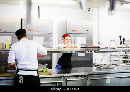 Femme souriante, chef, penchée au comptoir avec un étudiant qui travaille école de cuisine Banque D'Images