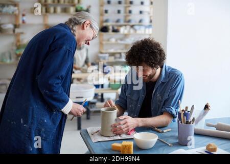 Souriant, des étudiants masculins et féminins apprennent la poterie en studio d'art Banque D'Images