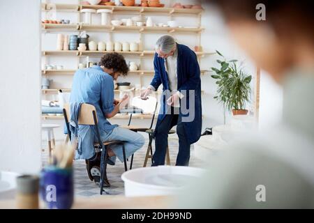 Souriant, des étudiants masculins et féminins apprennent la poterie en studio d'art Banque D'Images