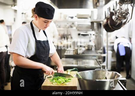 Jeune femme chef hacher des légumes sur la planche à découper en cuisine école Banque D'Images
