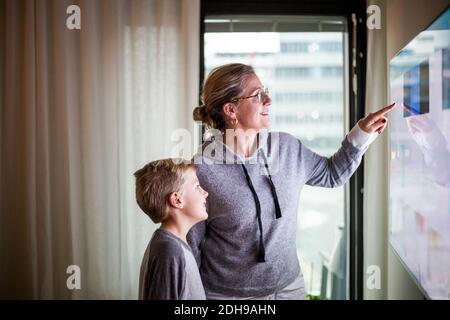 Mère guidant son fils dans l'utilisation de Smart TV à la maison Banque D'Images