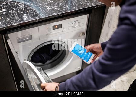 Image rognée de l'homme contrôlant le lave-linge avec l'application mobile chez vous Banque D'Images