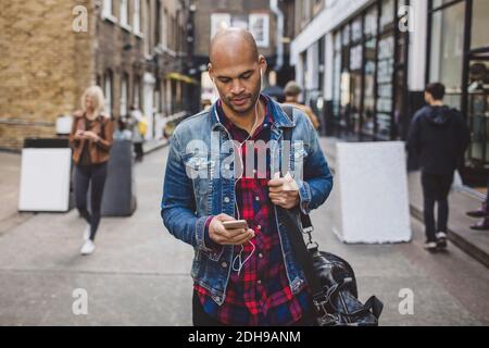 Homme de taille moyenne qui écoute de la musique sur un téléphone portable sur la route en ville Banque D'Images