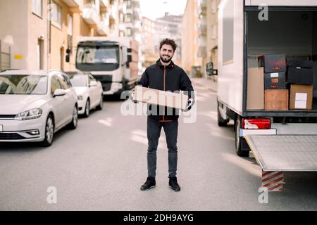 Portrait d'un jeune liveur confiant avec une boîte penchée chariot Banque D'Images