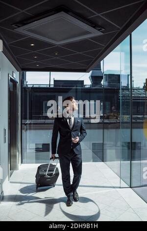 Homme d'affaires mature tirant des bagages à roulettes dans le couloir de l'hôtel Banque D'Images