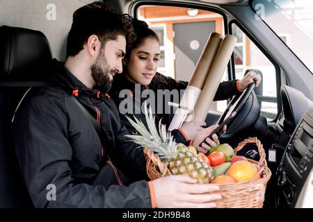 Jeune liveur homme et femme avec des fruits et des paquets dans chariot Banque D'Images