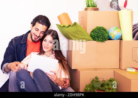 Un jeune couple heureux utilisant une tablette pour un nouveau projet de maison. Homme et femme assis près des boîtes en carton dans la nouvelle maison de propriété. Location, achat, style de vie et relatio Banque D'Images